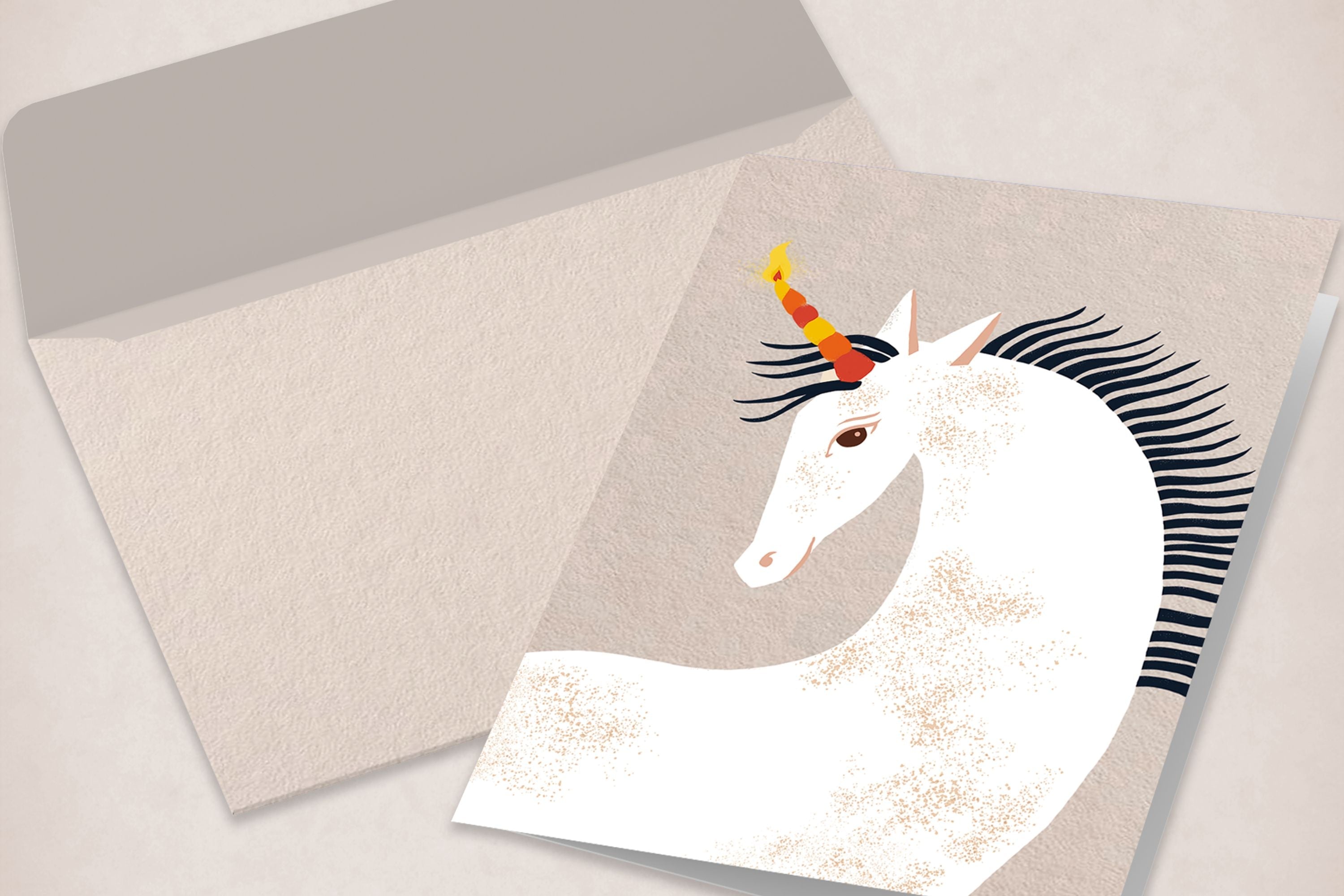 Offener Umschlag mit Grußkarte, darauf eine Illustration eines weißen Einhorns mit buntem Horn und schwarzer Mähne vor hellbeigem Hintergrund