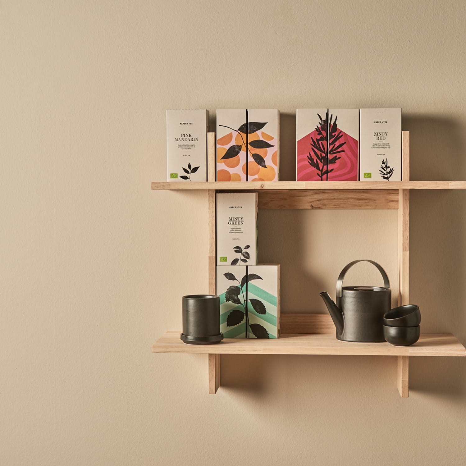 Minimalistisches Holzregal mit Papier & Tea Teeboxen: Pink Mandarin, Minty Green, Zingy Red, schwarze Teekanne, zwei Tassen.