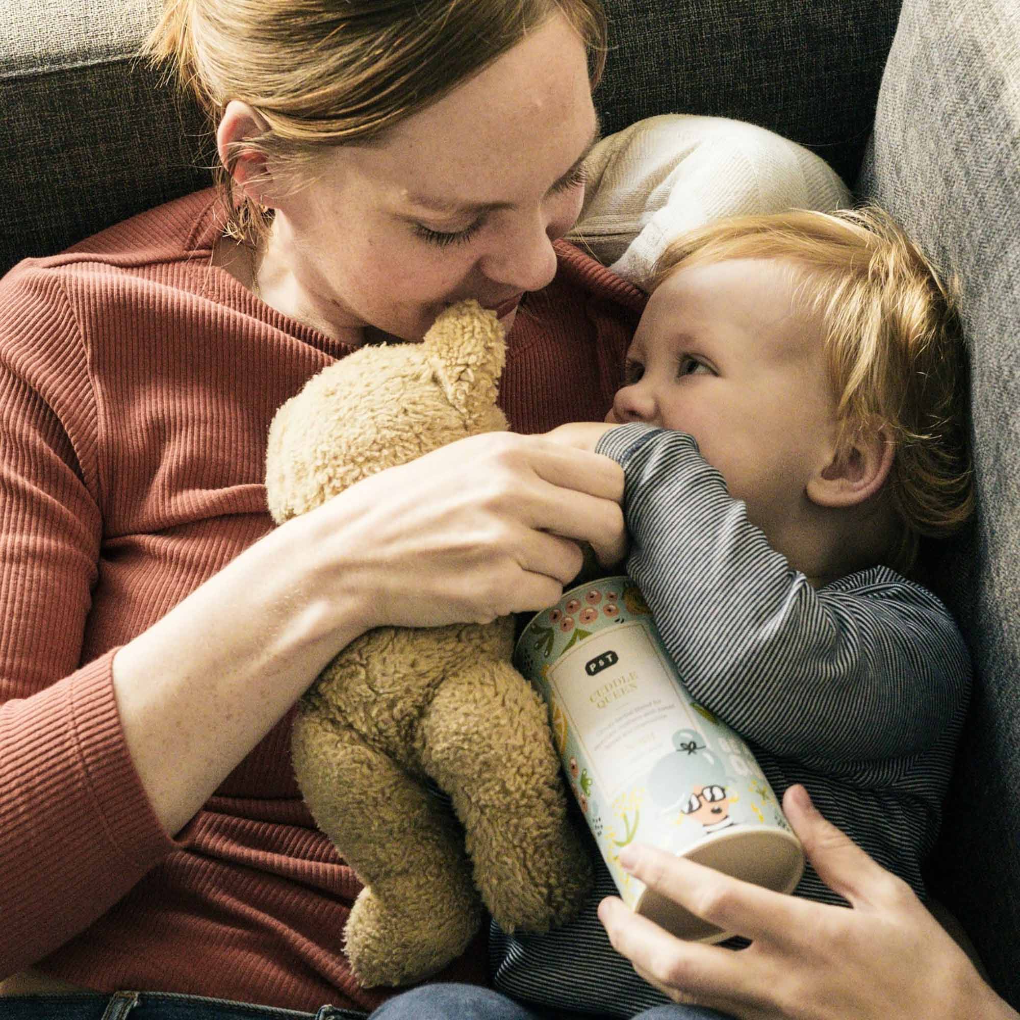 Frau in rostfarbenem Strickshirt hält Teddybär, während Kind mit gestreiftem Shirt P & T Cuddly Queen Dose umarmt.