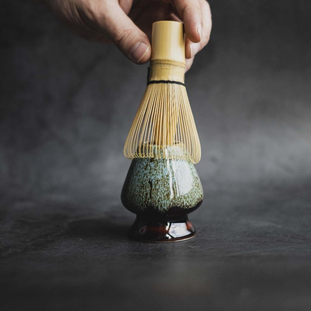 Hand mit Bambusbesen über gefleckter Keramikschale für Teezeremonie