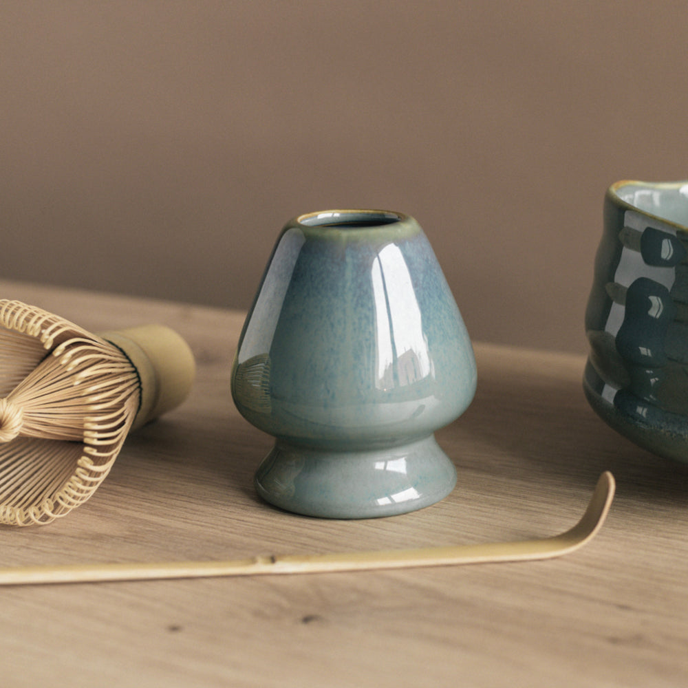 Traditionelle japanische Teezeremonie mit Keramikgefäß, Bambusbesen und Löffel auf Holztisch.