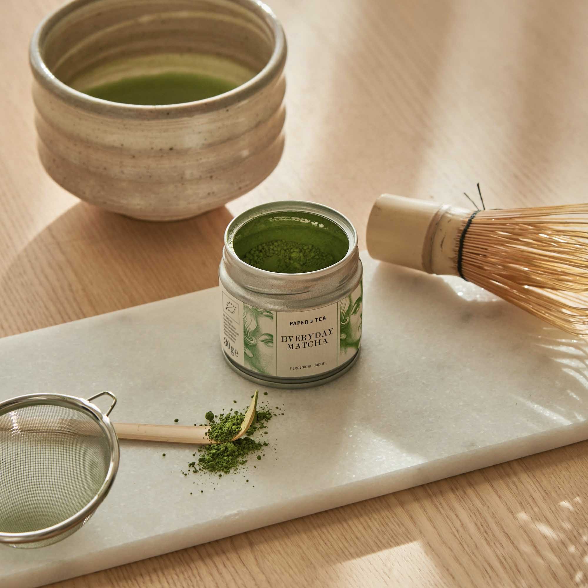 Metalldose mit grünem Matcha aus Kagoshima, Japan, auf Marmor mit Keramikschale, Bambusbesen und Löffel