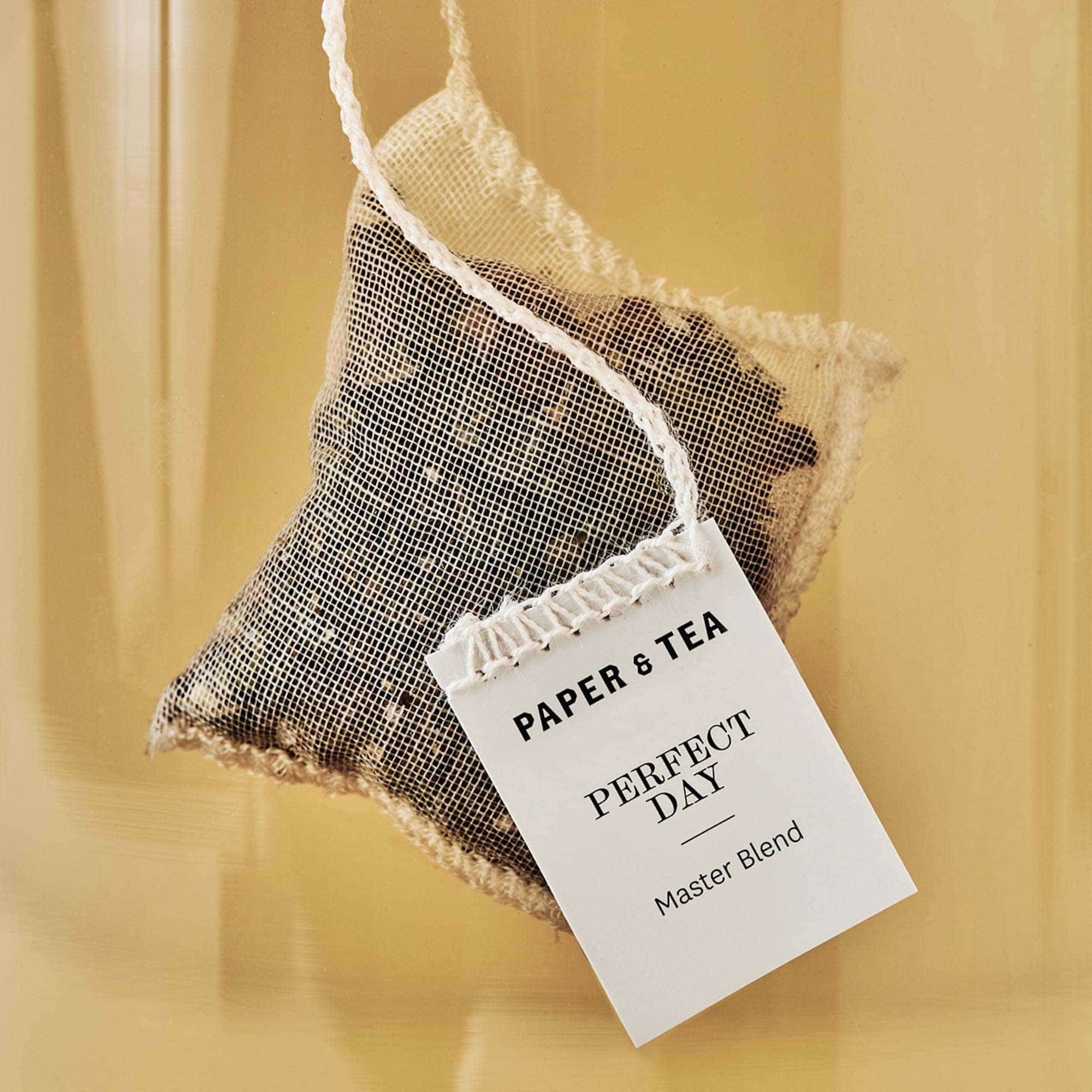 Weißer Netz-Teebeutel mit dunklem Blatttee, beschriftet als PAPER & TEA Perfect Day Master Blend.