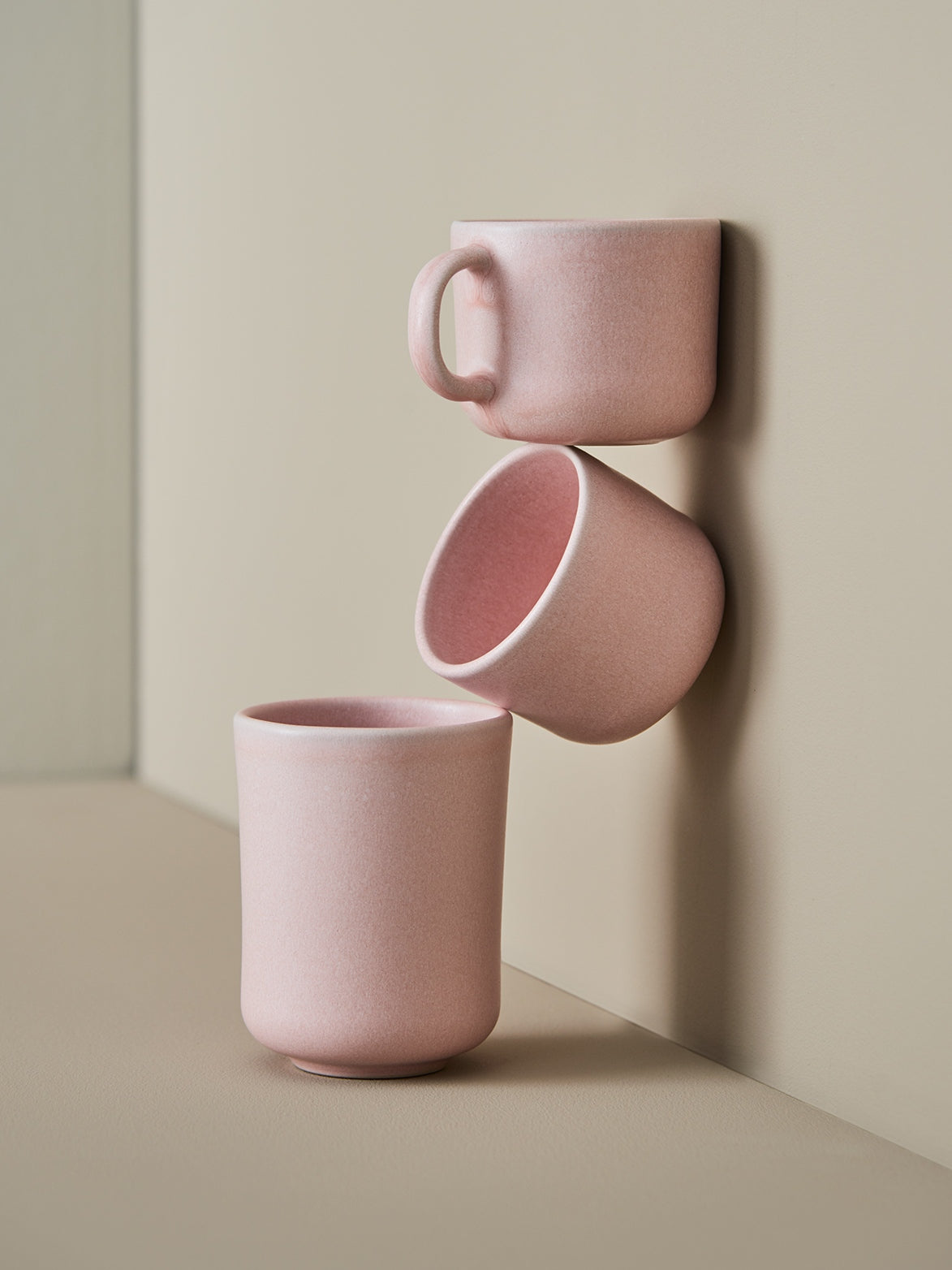Drei matte rosa Keramikbecher vor beiger Wand, minimalistisch und stilvoll angeordnet