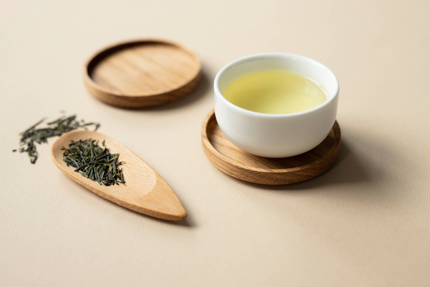 Weiße Tasse mit Grüntee auf Holzuntersetzer neben Holzlöffel mit losem Grüntee