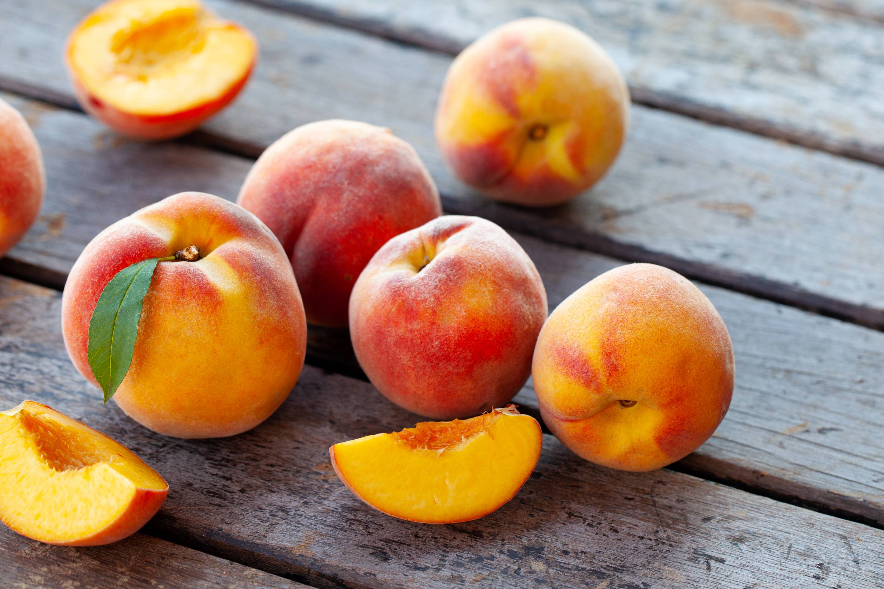 eife Pfirsiche mit samtiger Haut und Pfirsichscheiben auf Holzplatte
