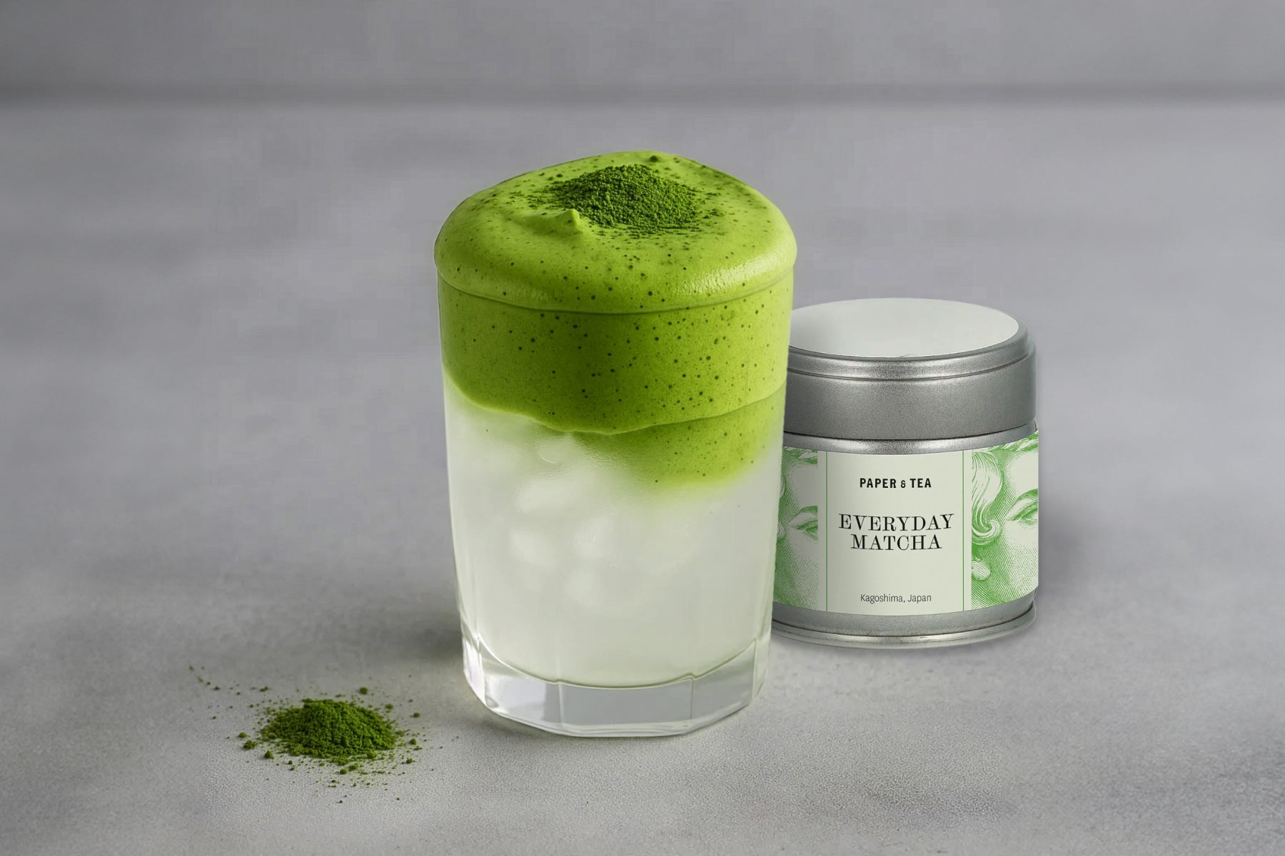 Glas mit eisgekühltem, geschichtetem Matcha und Kokosnusswasser, daneben Metalldose und Matcha-Pulver aus Kagoshima
