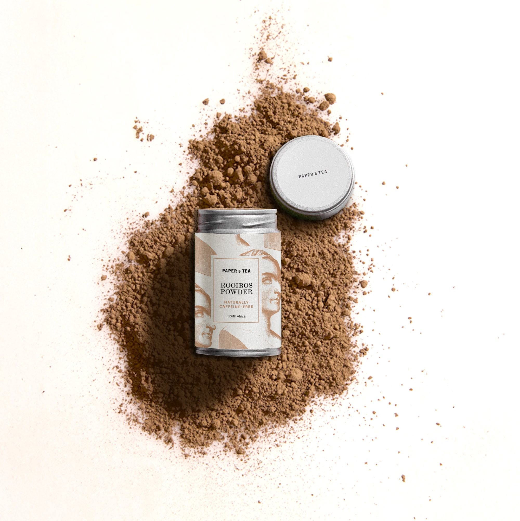 Elegante Dose mit Rooibos-Pulver von Paper & Tea, koffeinfrei, mit silbernem Deckel auf brauner Pulverschicht.