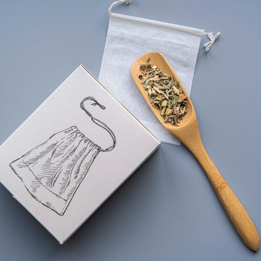 Holzlöffel mit getrocknetem Zitronengras auf Stoffbeutel neben Kräutertee-Verpackung.
