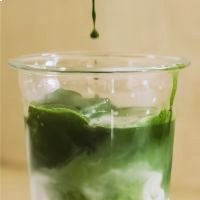 Ein transparentes Glas mit grünen und weißen Schichten, grüner Sirup tropft hinein.