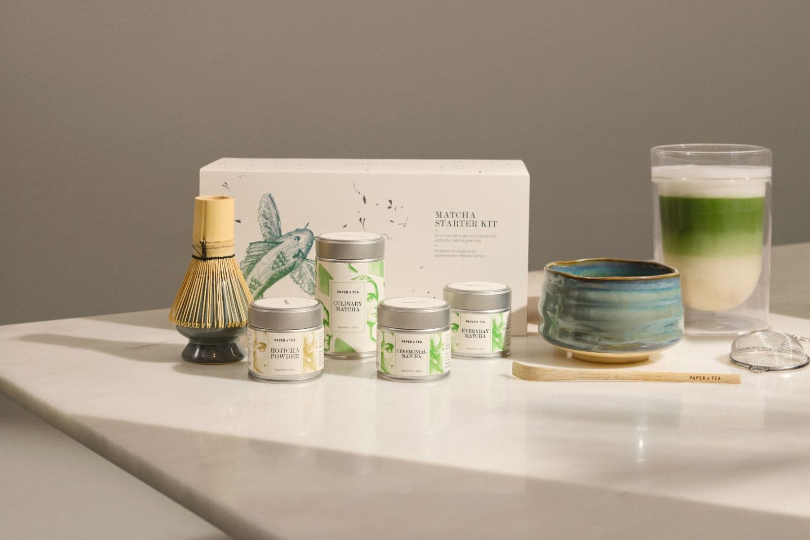 Elegantes Matcha-Starterkit mit Matcha-Dosen, Bambusbesen, Keramikschale, Holzlöffel, Glasschale und Metallsieb.