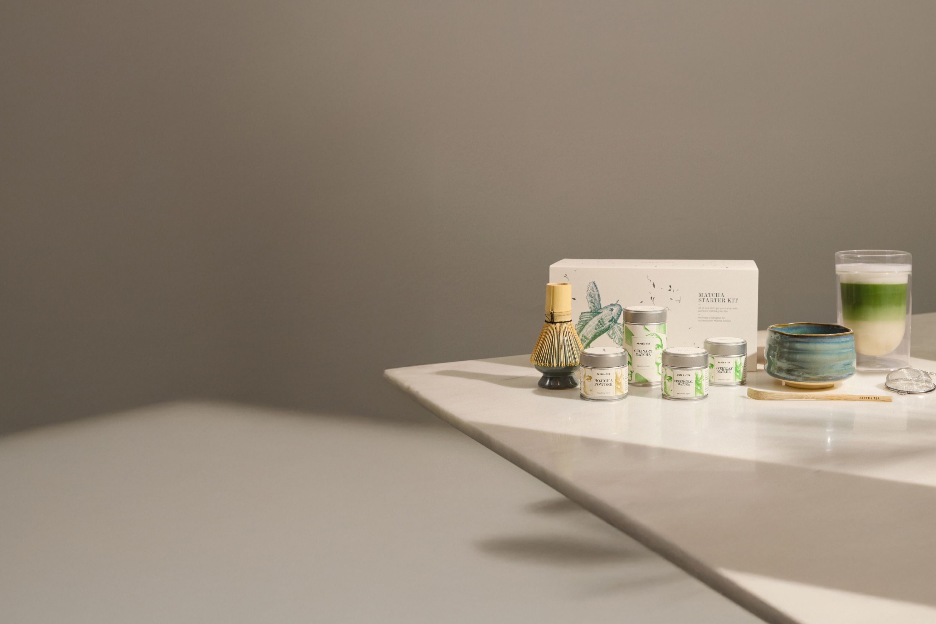 Matcha-Set mit Bambusbesen, Keramikschale, grünem Getränk, Holzlöffel und Teesieb auf Marmor