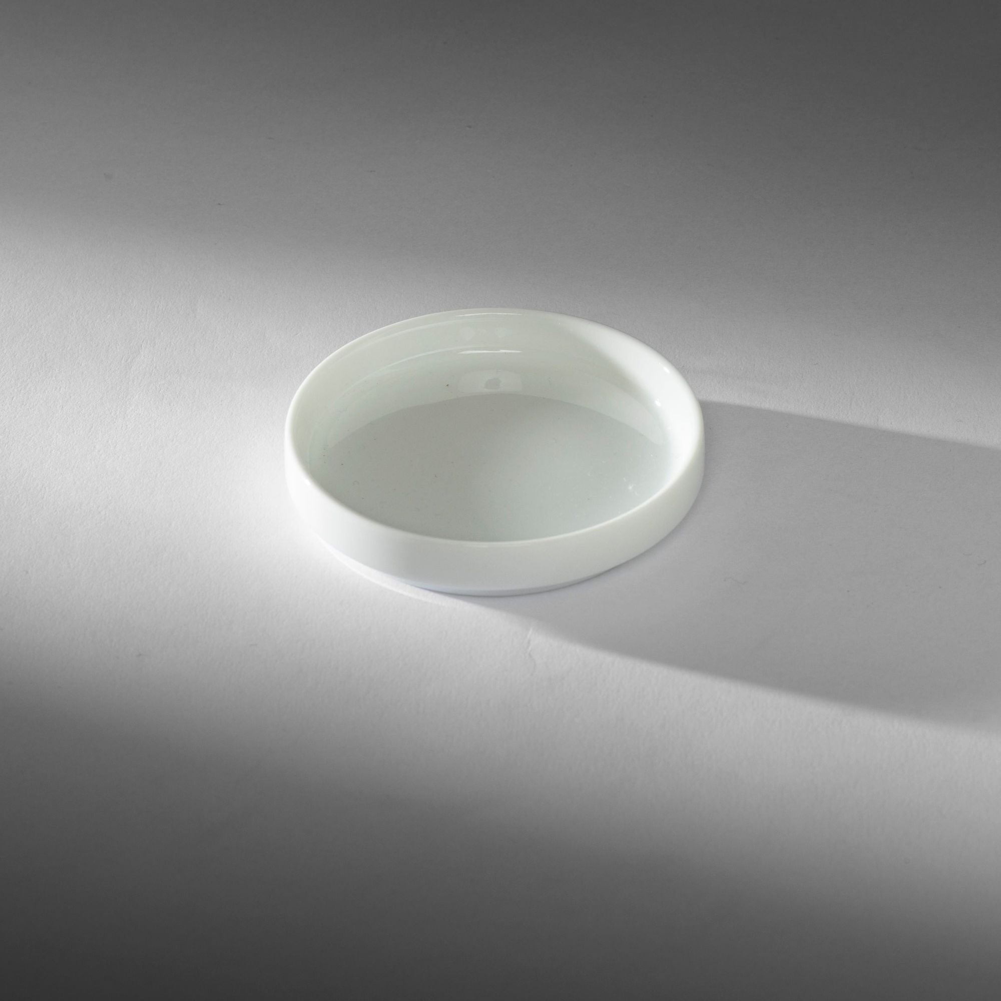Weiße Keramikschale mit grünem Tee auf hellem grauen Untergrund mit weichem Schatten.