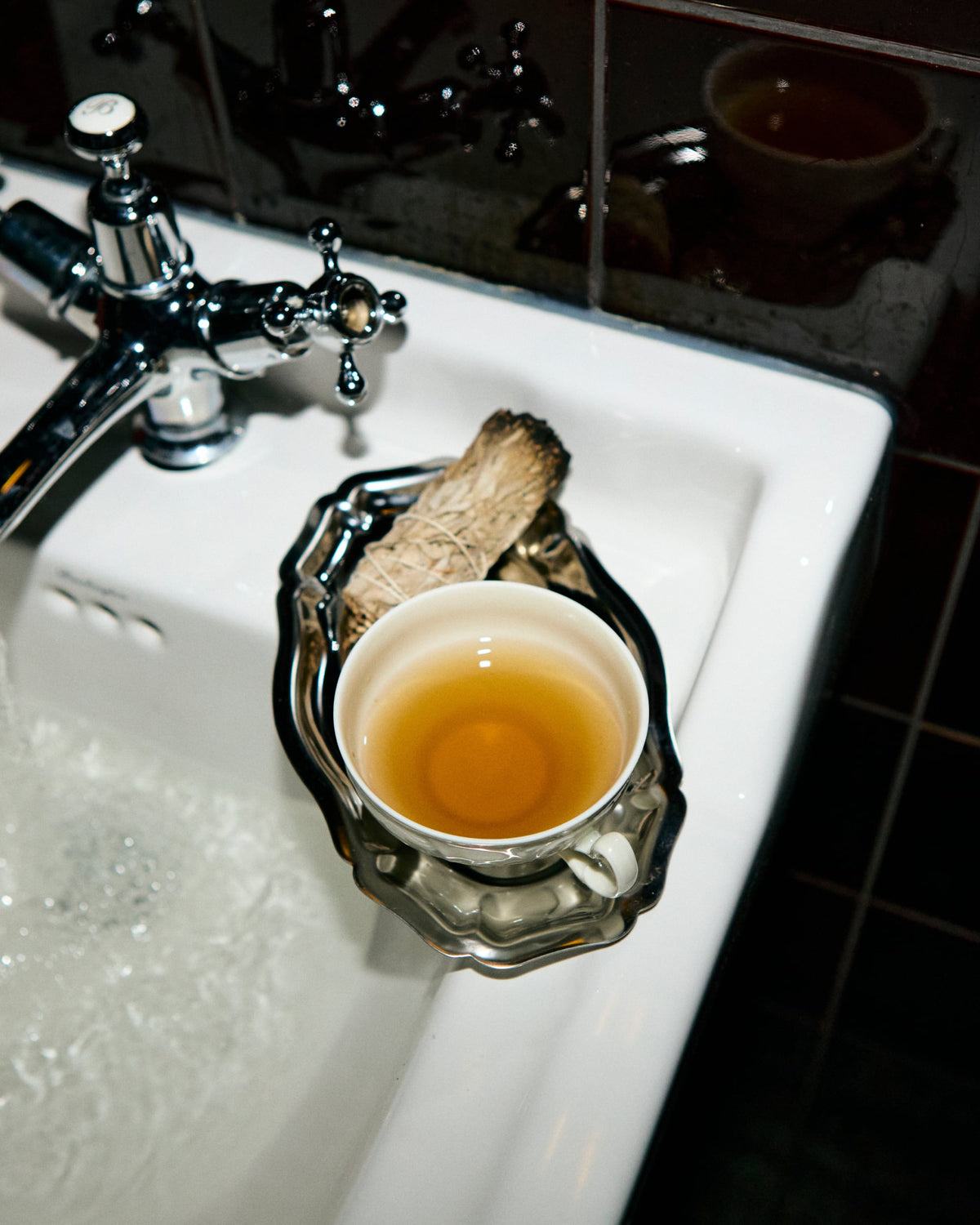 Weißes Keramikwaschbecken mit fließendem Wasser, silbernes Tablett mit Tee und getrockneten Kräutern