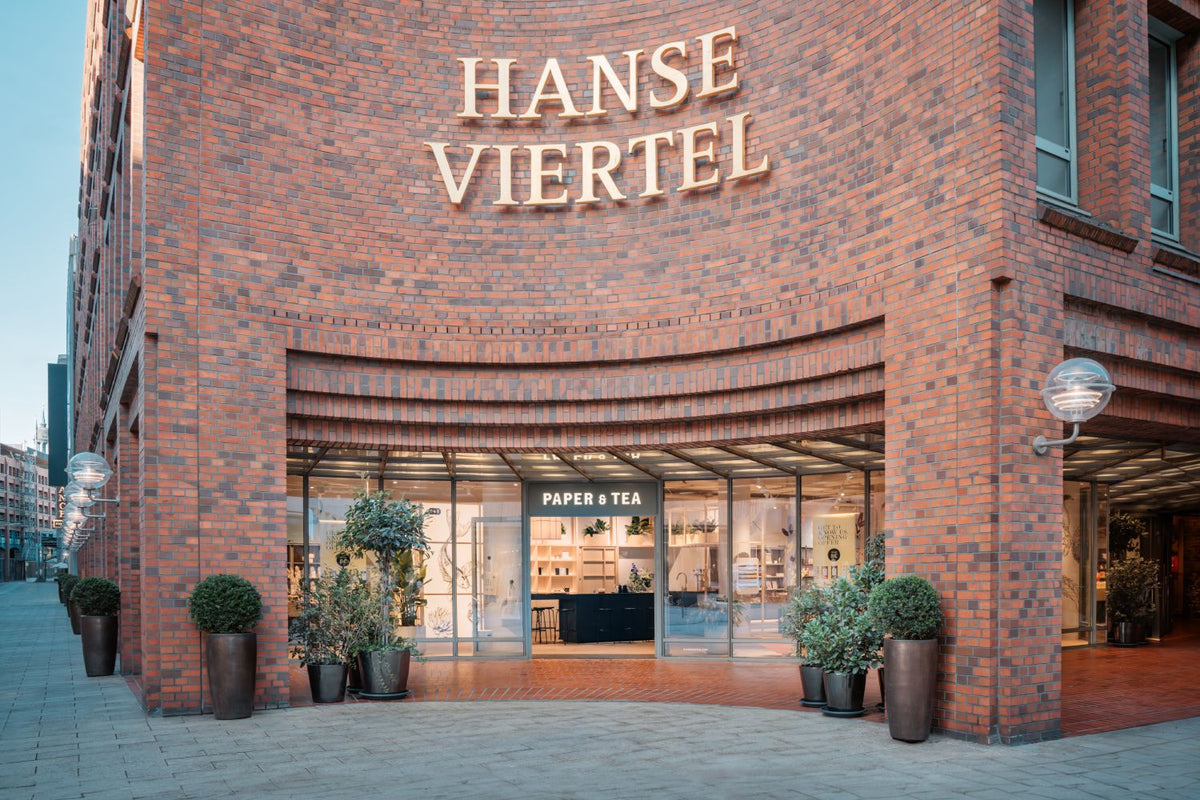 Paper & Tea Verkaufsstelle im HANSE VIERTEL mit beleuchteter Fassade und Pflanzen.