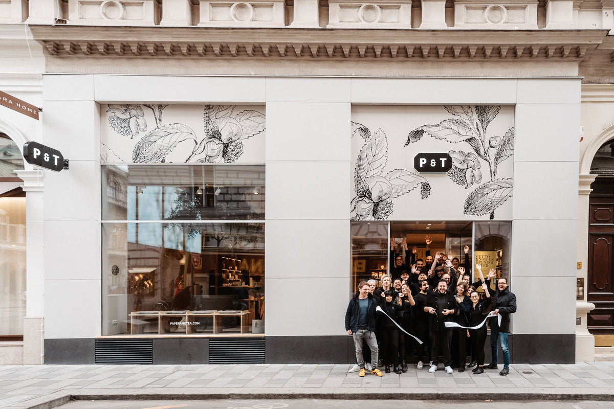 Menschen feiern die Eröffnung des P&T Ladens mit schwarzer Blumenfassade und großem Schaufenster.
